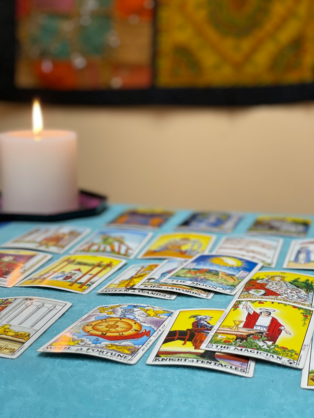 Tarotkort utspridda på en blå duk med ett ljus.