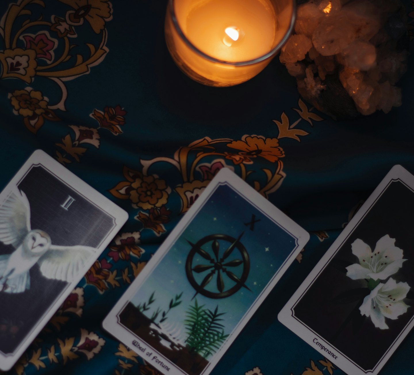 Tarotkort, ljus och kristaller på ett mönstrat tyg.
